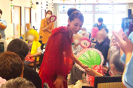 真っ赤なドレスで利用者様と握手をする美空えり子さん